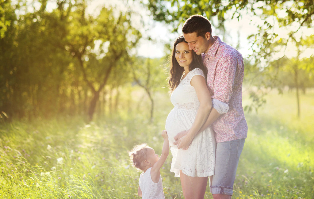 Happy pregnant family having fun in summer nature
